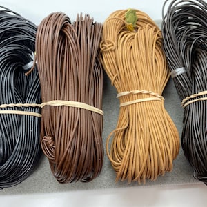 May include: Four spools of leather cord in black, brown, tan, and dark brown. The cords are wrapped around themselves and secured with rubber bands.