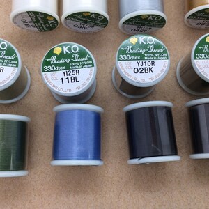 May include: Assortment of spools of K.O. Beading Thread in various colours, including green, blue, black, brown, and white. Each spool is labelled with the brand name, thread type, and colour code.