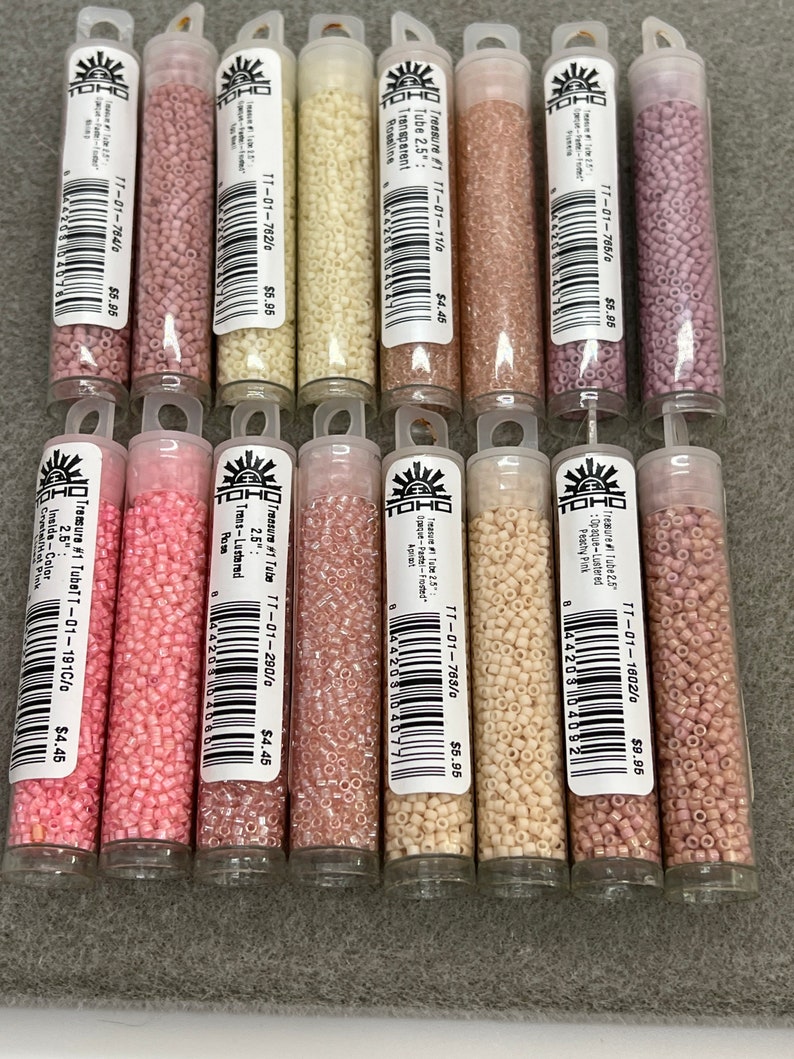 May include: A selection of Toho Treasure seed beads in shades of pink, peach, and cream, presented in clear plastic tubes. Each tube is labelled with product details, including colour and size, and the price.