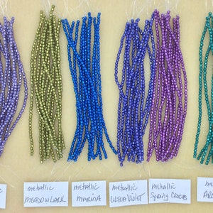 May include: Six strands of metallic beads in various colors, including purple, green, blue, and teal. The beads are labeled with their color names: Metallic Crocus, Meadow Lark, Marina, Ultra Violet, Spring Crocus, and Arcadia.