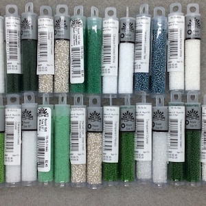 May include: A collection of 20 small tubes of TOHO seed beads in various colors, including green, white, and blue. The tubes are labeled with the bead size, color, and TOHO brand name.