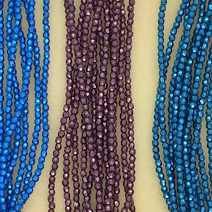 May include: Three strands of faceted metallic beads. One strand is blue, one is purple, and one is teal.