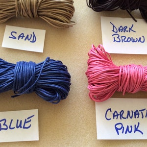 May include: Four spools of waxed cotton cord in different colors: sand, blue, carnation pink, and dark brown. Each spool is labeled with its color.