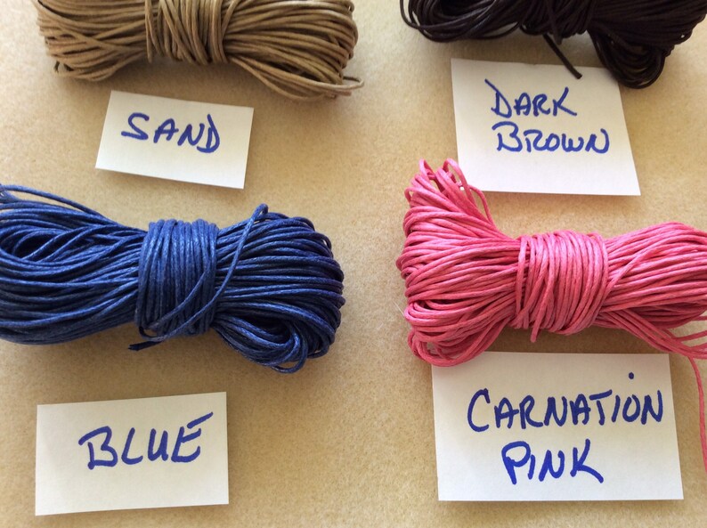 May include: Four spools of waxed cotton cord in different colors: sand, blue, carnation pink, and dark brown. Each spool is labeled with its color.