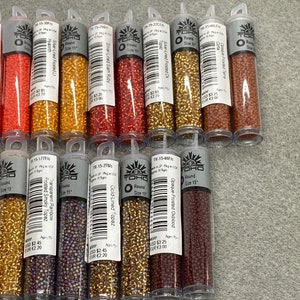 May include: A collection of 12 small tubes of assorted colors of seed beads. The tubes are labeled with the bead size, color, and brand name "TOHO".