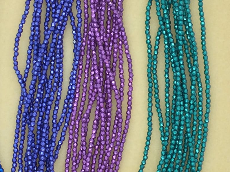 May include: Three strands of faceted glass beads in blue, purple, and teal colors. The beads are small and have a metallic sheen.