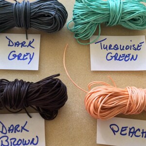 May include: Four spools of waxed cotton cord in different colors: dark grey, dark brown, turquoise green, and peach. The spools are labeled with their respective colors.