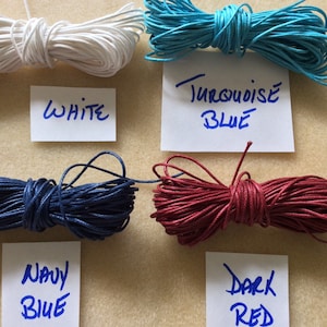 May include: Four spools of waxed cotton cord in white, turquoise blue, navy blue, and dark red. Each spool is labeled with the color name.