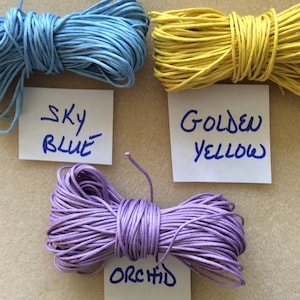 May include: Three spools of waxed cotton cord in sky blue, golden yellow, and orchid colors. Each spool is labeled with the color name.