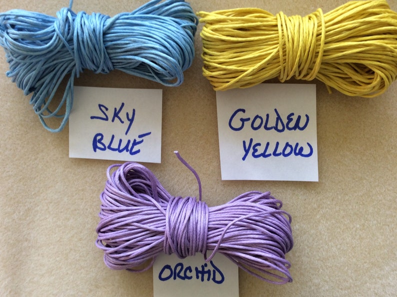 May include: Three spools of waxed cotton cord in sky blue, golden yellow, and orchid colors. Each spool is labeled with the color name.
