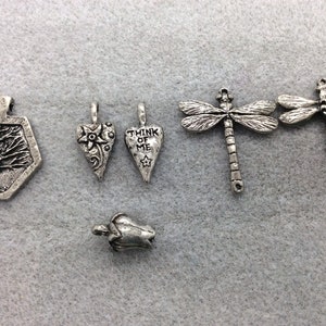 May include: A set of six silver charm pendants, including a tree, a heart with the text "Think of Me", a flower, a dragonfly, and a bell.