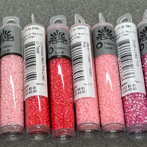 May include: Six clear tubes filled with small, colourful beads. The tubes are labelled with the brand "TOHO Treasure Size #1" and various shades of pink, including "Ceylon Innocent Pink" and "Silver-Lined Pink".