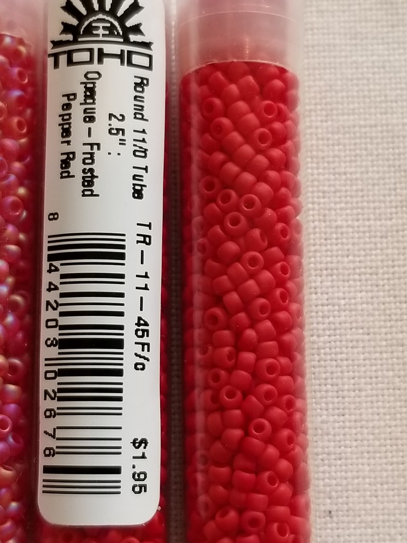 Pode incluir: Um pequeno tubo de contas de sementes vermelhas, opacas e foscas. O tubo est&aacute; etiquetado "TOHO Round 11/0 Tube TR-11-45 F/c 2.5" Pepper Red 1,95 &euro;".