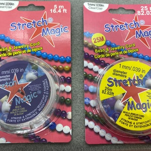 May include: Two packages of clear elastic bead and jewelry cord. The packages are pink and feature a red star with the text "Stretch Magic" and the cord's diameter and length in inches and feet. The cord is wound around a clear spool.