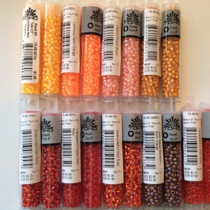 May include: A collection of 10 small tubes of TOHO brand round seed beads in various shades of orange and red. The tubes are labeled with the bead color, size, and product code.