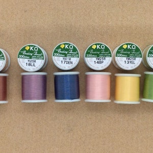 May include: Six spools of K.O. Beading Thread in a variety of colours, including copper, purple, blue, pink, yellow, and green. Each spool is labelled with the thread's colour code, lot number, and material.