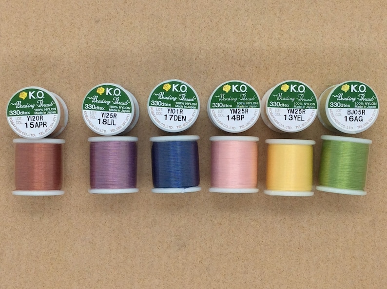 May include: Six spools of K.O. Beading Thread in a variety of colours, including copper, purple, blue, pink, yellow, and green. Each spool is labelled with the thread's colour code, lot number, and material.