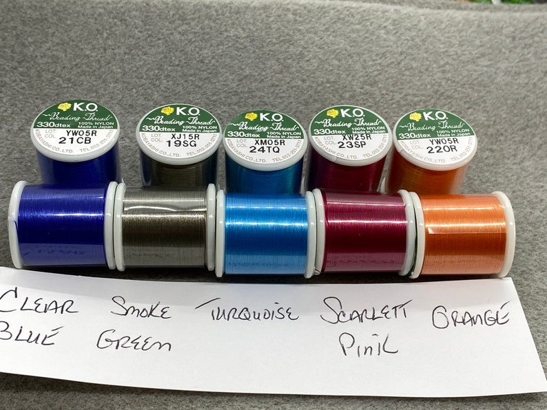 May include: Six spools of beading thread in various colours, including clear blue, smoke green, turquoise, scarlet pink, and orange. Each spool is labelled with the brand "KO Beading Thread" and a lot number.