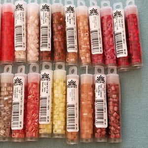 May include: A collection of 16 small tubes of TOHO seed beads in various colors, including red, pink, brown, and yellow. Each tube is labeled with the bead size, color, and product code.