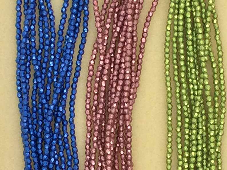 May include: Three strands of metallic beads in blue, pink, and green. The beads are small and have a faceted, shiny finish.