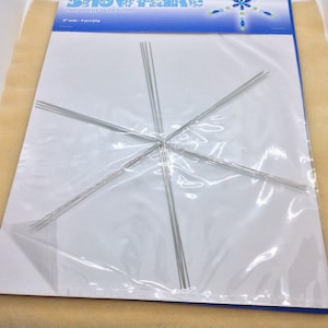 Puede incluir: Un paquete de Beadsmith Snowflake Ornament Wire Form. El paquete es azul y blanco y muestra un copo de nieve hecho de cuentas. La forma de alambre está dentro de una bolsa de plástico transparente.