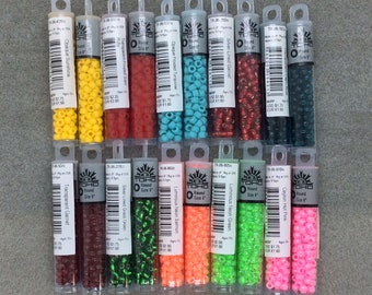 May include: Assortment of 12 small glass beads in various colors, including yellow, red, turquoise, silver, green, brown, and pink. The beads are packaged in clear plastic tubes with labels that include the color name, size, and price. The beads are labeled as TOHO Round Size 6.