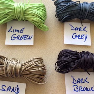 May include: Four spools of waxed cotton cord in different colors: lime green, dark grey, sand, and dark brown. Each spool has a handwritten label with the color name.