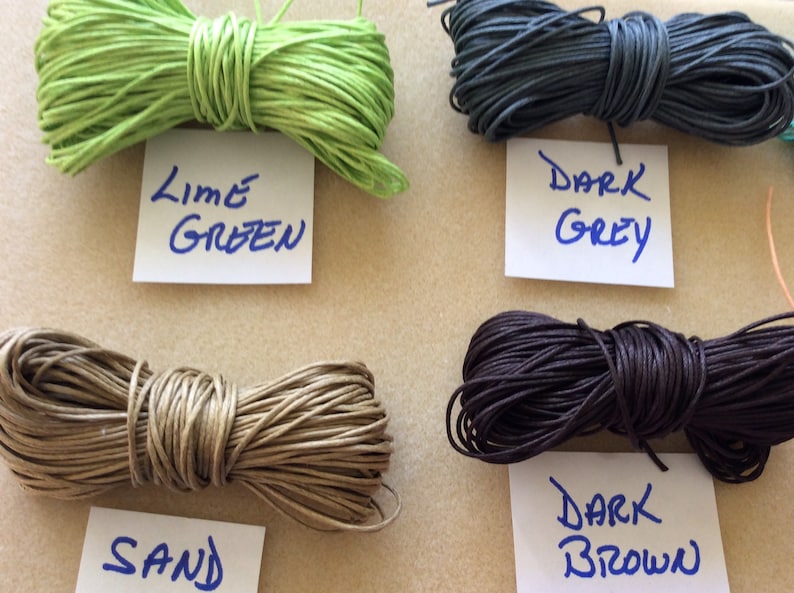 May include: Four spools of waxed cotton cord in different colors: lime green, dark grey, sand, and dark brown. Each spool has a handwritten label with the color name.