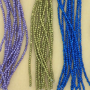 May include: Four strands of faceted glass beads in purple, green, blue, and purple. The beads are small and have a metallic sheen.