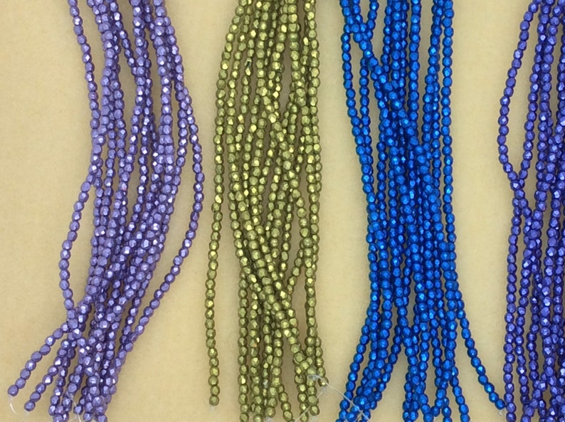 May include: Four strands of faceted glass beads in purple, green, blue, and purple. The beads are small and have a metallic sheen.