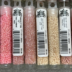 May include: A selection of small, cylindrical beads in clear plastic tubes. The beads are various shades of pink, peach, and cream. Each tube has a label with text including "Treasure #1 Tube" and colour descriptions. The beads are 6.35 cm long.