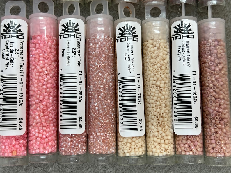 May include: A selection of small, cylindrical beads in clear plastic tubes. The beads are various shades of pink, peach, and cream. Each tube has a label with text including "Treasure #1 Tube" and colour descriptions. The beads are 6.35 cm long.