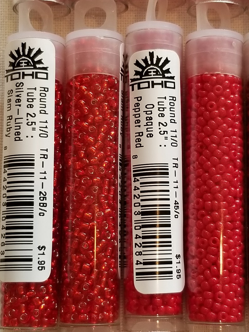 Pode incluir: Tr&ecirc;s tubos de contas de semente vermelhas TOHO. Os tubos s&atilde;o etiquetados com o tamanho das contas, a cor e o pre&ccedil;o. As contas s&atilde;o de tamanho 11/0 e v&ecirc;m em um tubo de 2,5 polegadas. As cores s&atilde;o Vermelho Pimenta, Rubi Slam e Rubi Slam Forrado de Prata.