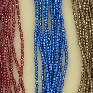 May include: Three strands of metallic beads, one red, one blue, and one gold. The beads are faceted and have a shiny finish.