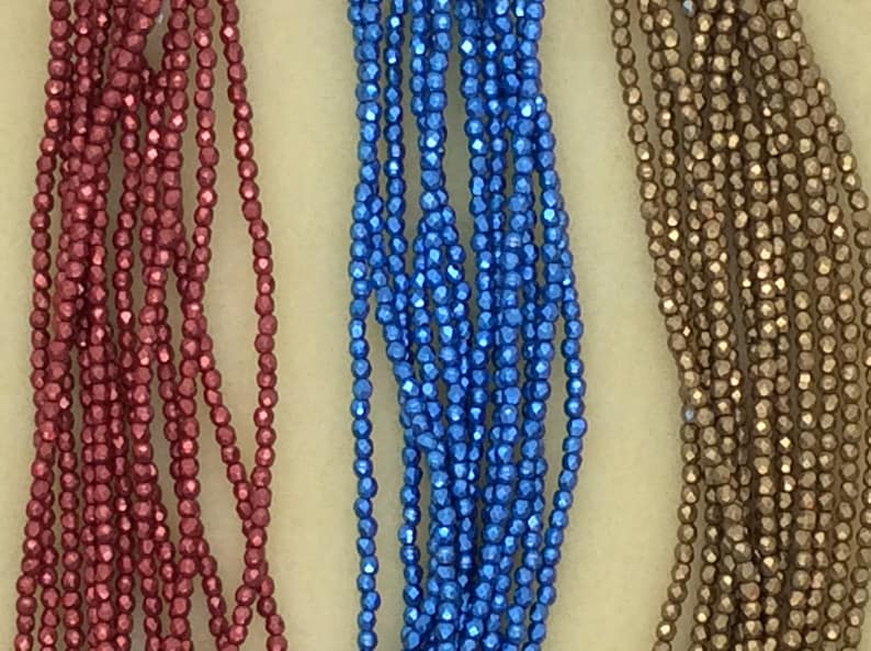 May include: Three strands of metallic beads, one red, one blue, and one gold. The beads are faceted and have a shiny finish.
