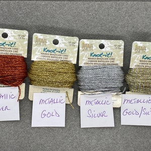 May include: Four spools of waxed Brazilian cord, each 15 yards long. The cords are metallic copper, gold, silver, and a gold and silver mix. The spools are labeled "Knot-it!" and "Bead Smith".