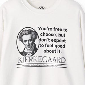 Puede incluir: Camiseta blanca de manga larga con una ilustración en blanco y negro de un hombre y una cita que dice "You're free to choose, but don't expect to feel good about it. KIERKEGAARD Philosophy for People Who Just Want the CliffNotes!"