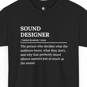 May include: A black short-sleeved t-shirt featuring white text that defines a sound designer as the person who decides what the audience hears, what they don't, and why that perfectly timed silence matters just as much as the sound.