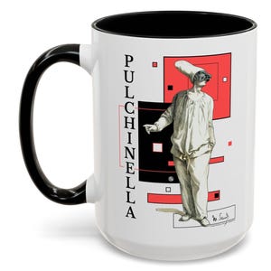 May include: White ceramic mug with a black handle and interior. The mug features a graphic of a figure in a white costume and mask, with the word "PULCHINELLA" printed vertically. Red and black geometric shapes are in the background.