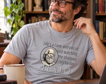 May include: A heather gray short-sleeve t-shirt featuring a circular illustration of Plato with the text: Life's a cave, and you're just watching the shadows -try harder.. PLATO Philosophy: The Reader's Digest Condensed Version.