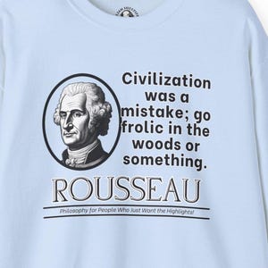Puede incluir: Camiseta azul claro con una ilustración en blanco y negro de Jean-Jacques Rousseau. El texto "Civilization was a mistake; go frolic in the woods or something." y "ROUSSEAU" está impreso en la camiseta. El texto "Philosophy for People Who Just Want the Highlights!" está impreso debajo de la ilustración.
