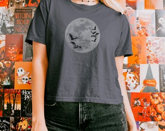 May include: A charcoal gray short-sleeve t-shirt featuring a circular graphic of a full moon with several small black bats flying across its surface. The shirt has a crew neckline and a straight hem, providing a standard fit for casual wear.