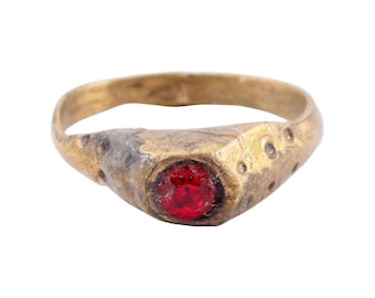 May include: A gold ring with a red gemstone set in the center. The ring has a worn, antique look.