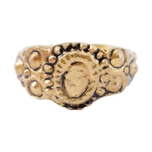 Op de afbeelding: Een gouden ring met een getextureerd ontwerp met een centraal ovaal omgeven door kleinere cirkels. De ring heeft een versleten, antieke uitstraling.