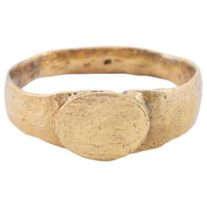 Puede incluir: Un anillo de sello de oro con un bisel redondo y liso. El anillo está desgastado y tiene una superficie texturizada.