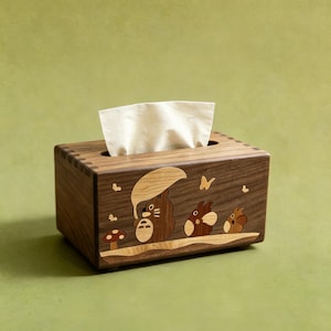 May include: A rectangular wooden tissue box holder featuring an inlaid wood design of three forest creatures, one holding an umbrella, alongside a small mushroom and butterflies. The box has visible finger joints at the corners and holds white tissues.