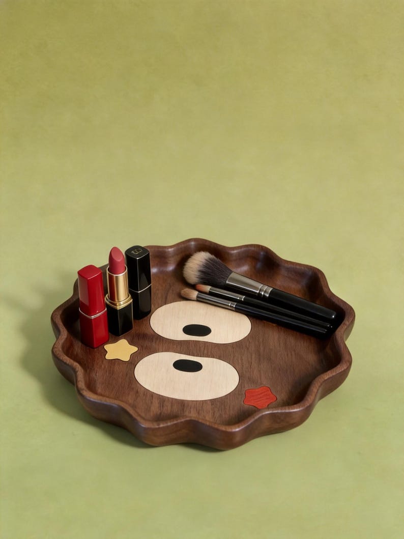 May include: A decorative wooden makeup tray with a cartoon face design. The tray has a wavy edge and features a cartoon face design with two large eye shapes and a red lip. It holds three lipsticks and several makeup brushes.