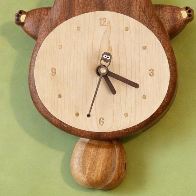 May include: A wooden wall clock shaped like a beaver with a light-coloured circular face. The clock features dark brown wooden arms and a tail, with numbers 3, 6, 9, and 12. The clock hands include a small, brown, fuzzy creature figure.