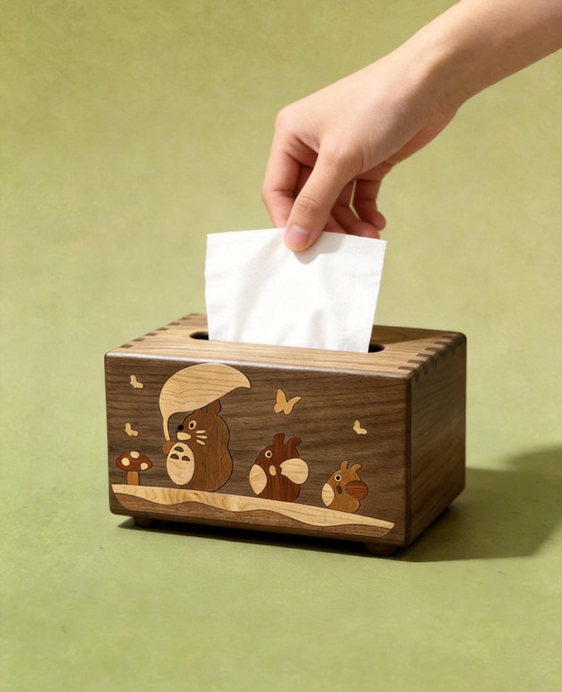 May include: A rectangular wooden tissue box holder featuring a dark brown wood grain finish. The front panel displays an inlaid wood design of three small creatures, one holding an umbrella, alongside a mushroom and butterflies.