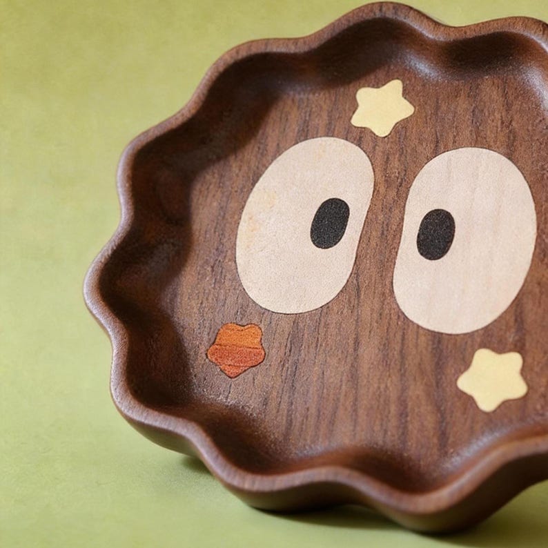 May include: A wooden tray with a wavy edge, featuring an owl design. The tray is brown with light tan eyes, black pupils, and an orange beak. Yellow star accents are placed around the eyes. The tray is likely used for serving or display.